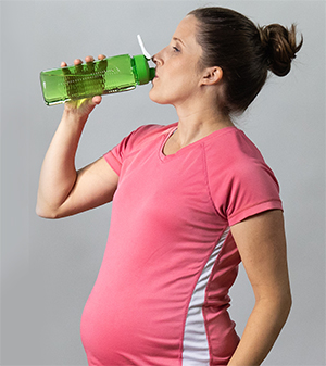 Una mujer embarazada bebiendo agua luego de hacer actividad física.